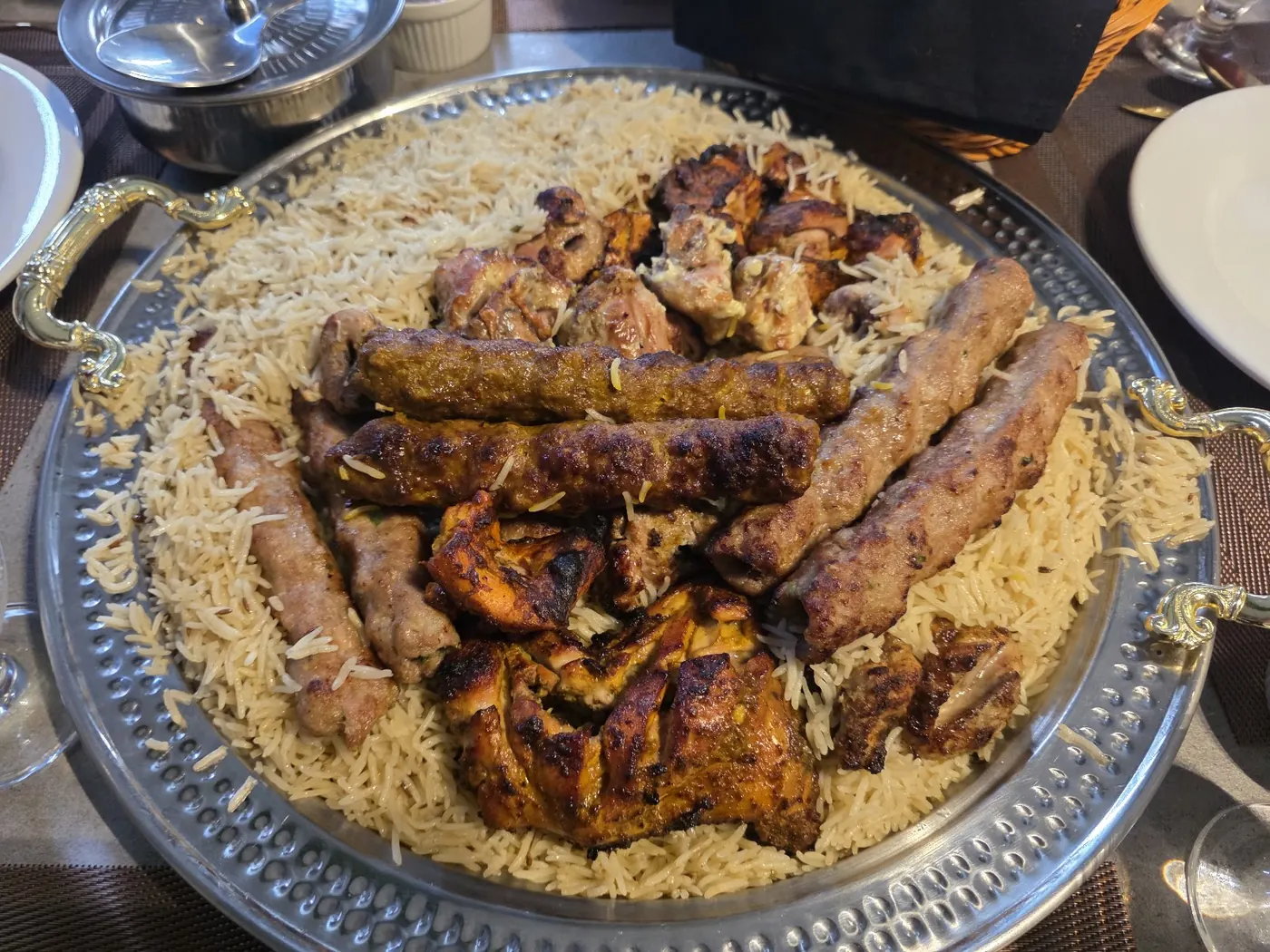 A Royal Sofra platter of seekh kababs, boti and grilled chicken over rice, with naan and sauces